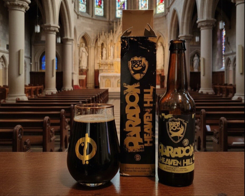 Bouteille de Paradox Heaven Hill de Brewdog avec sa boite à gauche pour finir tout à gauche avec le verre rempli. Tout est dans une église.