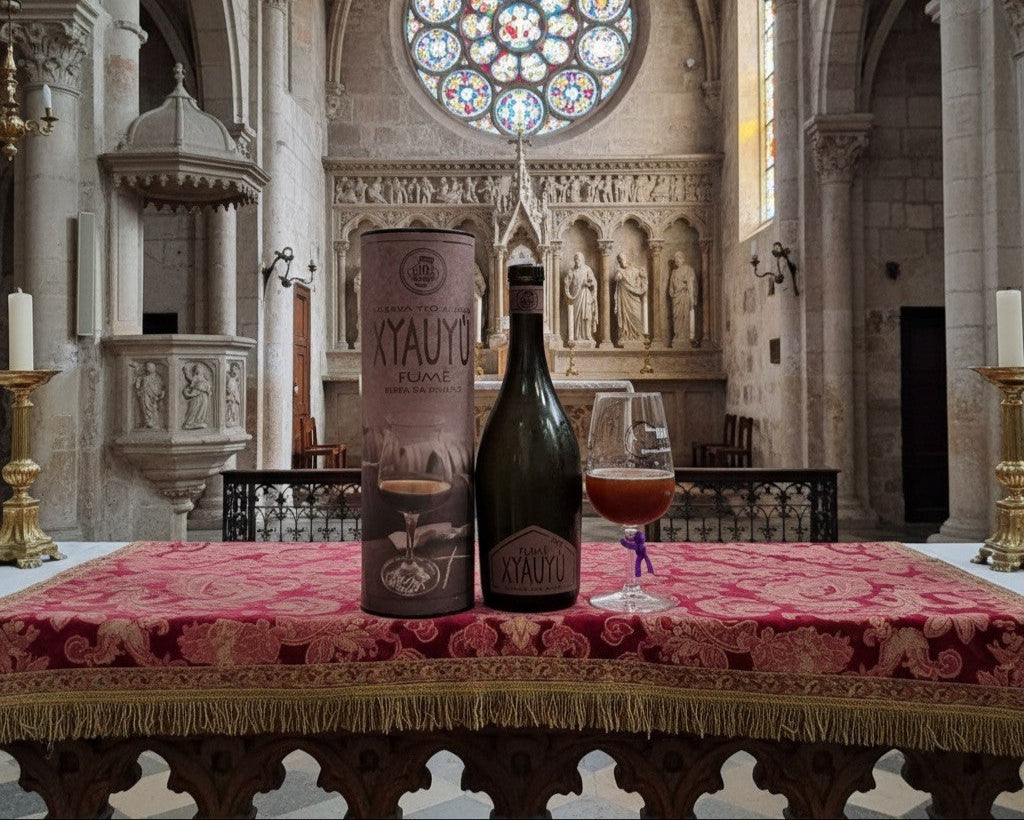 Bouteille de XYAUYÙ FUMÈ RISERVA 2011 de Baladin posée dans une église avec un verre à droite et sa boite à gauche.